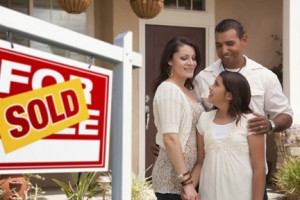 Hispanic Mother, Father and Daughter in Front of Their New Home with Sold Home For Sale Real Estate Sign. Hispanic Mother, Father and Daughter in Front of Their New Home with Sold Home For Sale Real Estate Sign.