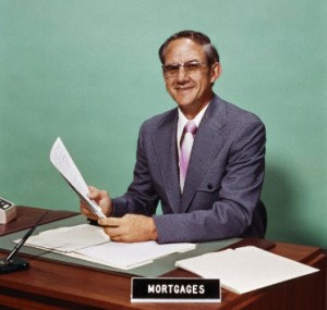 Man at desk holding papers with mortgage officer sign 