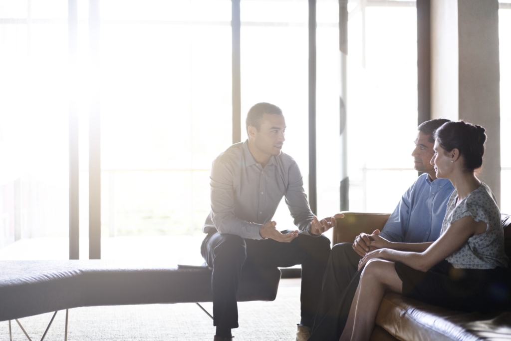 Young businessman talking with couple. Male financial planner explaining investment plans to clients. They are in office.