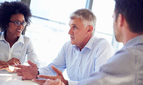 Three people are seated at a table talking.